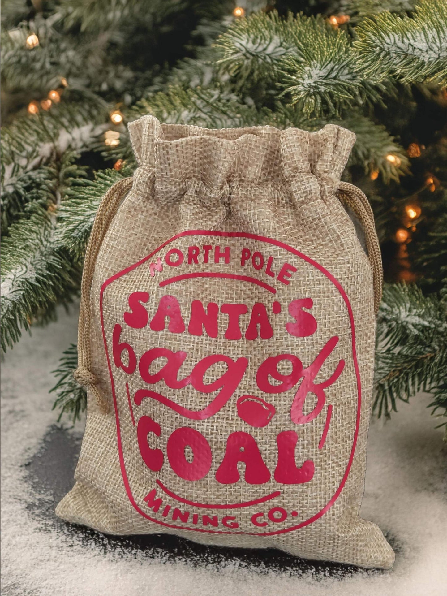 Personalized hessian bag of coal for Christmas gag gift under festive tree.