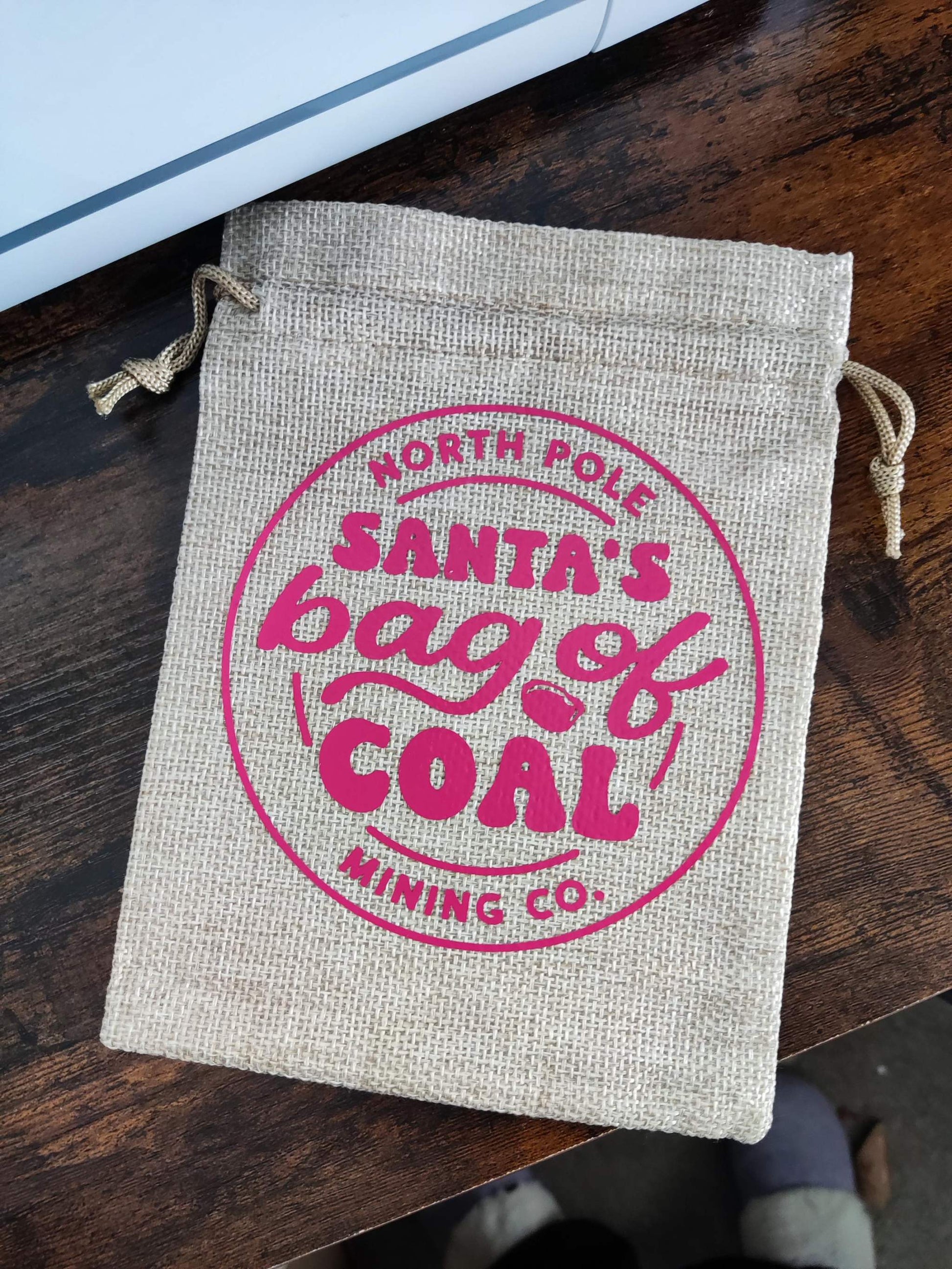 Personalized humorous "Bag of Coal" Christmas hessian sack on a wooden surface.